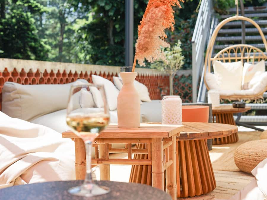A cozy outdoor seating area with a wicker chair, a round wooden table, and a vase with a dried plant.