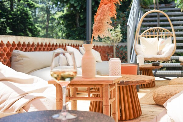 Un espace de détente extérieur accueillant, avec un fauteuil en osier, une table ronde en bois et un vase contenant une plante séchée.