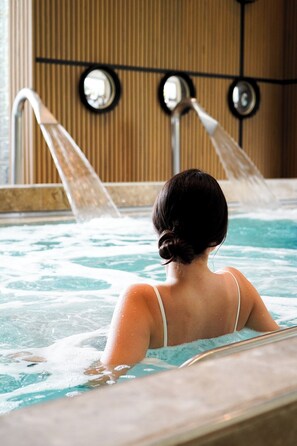 A person in a hot tub with water jets, a wooden wall with vertical slats, and a metal railing.