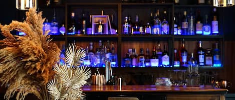 A bar area with a wooden counter, a vase with dried flowers, and shelves stocked with bottles.