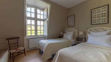 A bedroom with two beds, a wooden chair, a window, and a framed picture on the wall.
