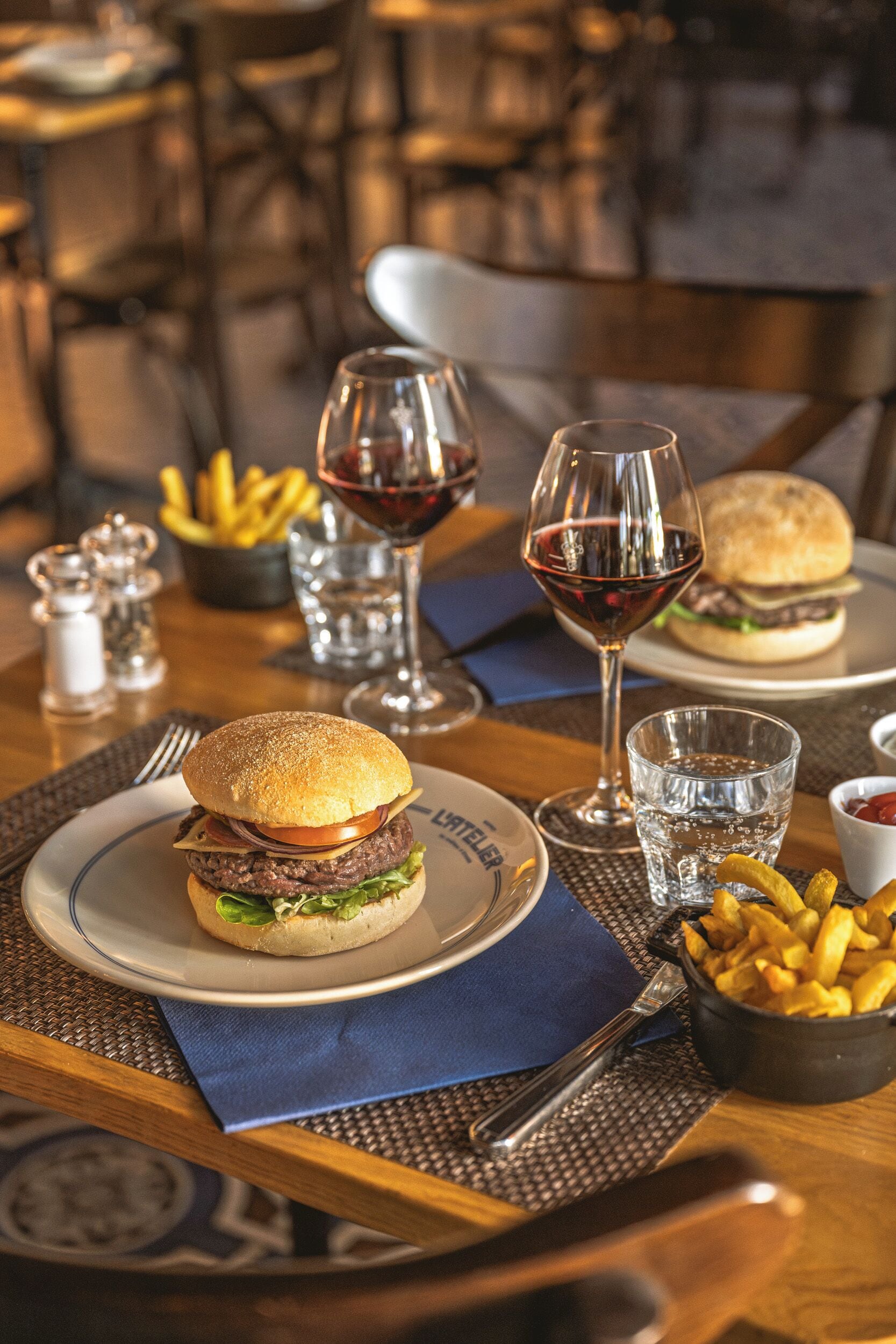 Una mesa de comedor con una hamburguesa, papas fritas y copas de vino.