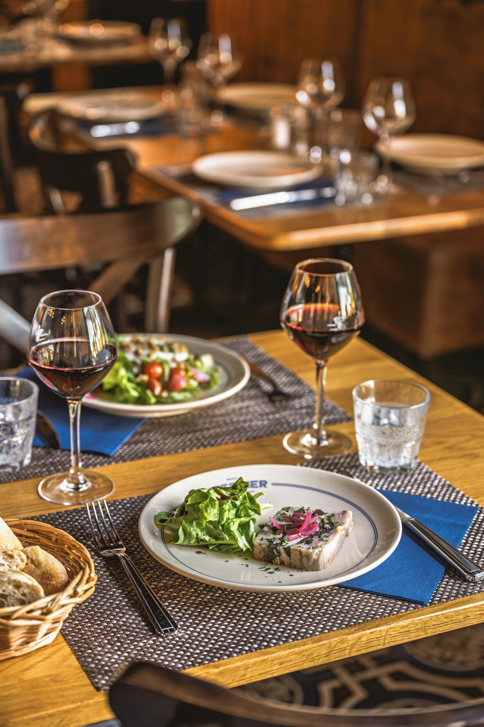 A dining table set with plates, glasses, and cutlery, a basket of bread, and a bottle of water.