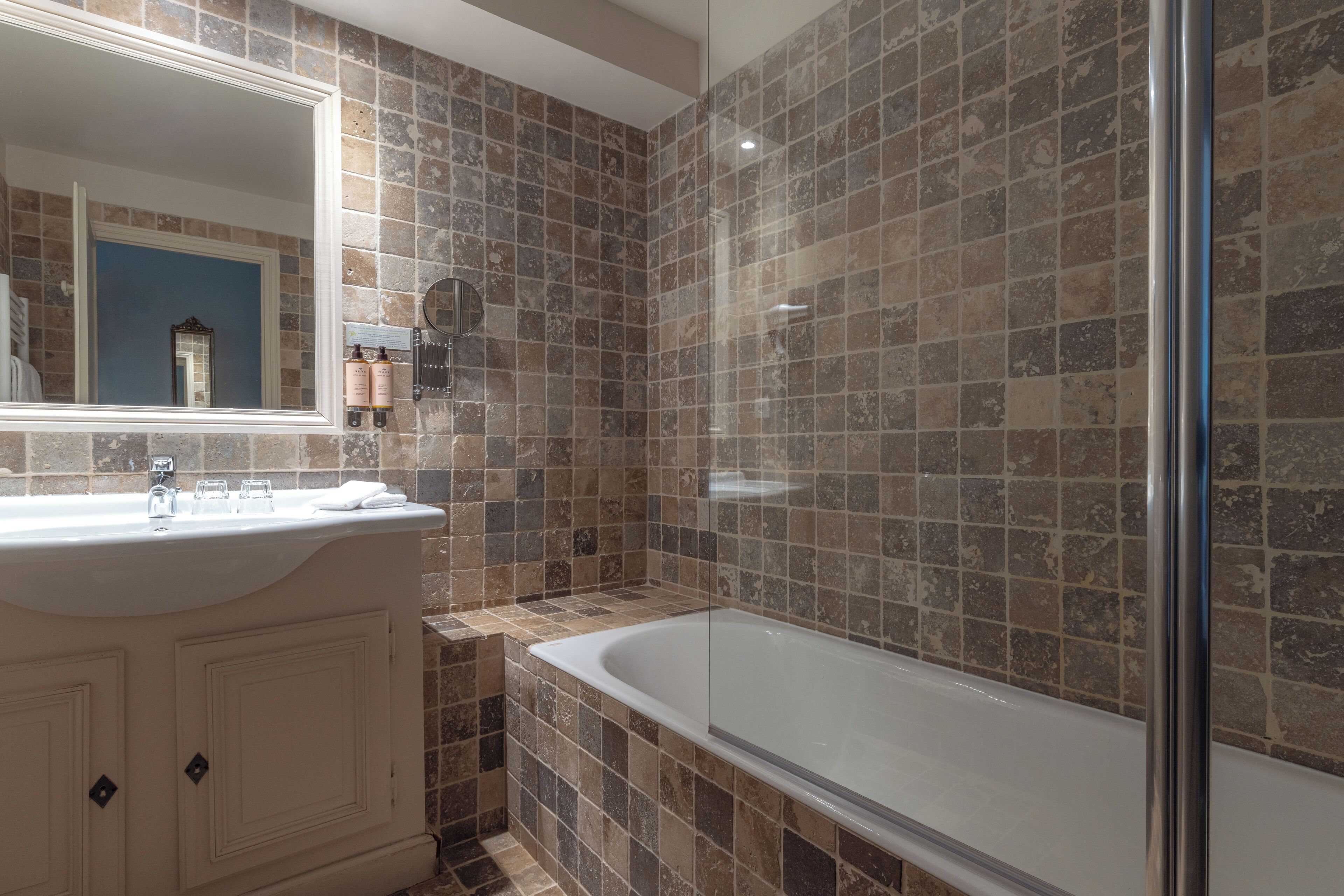 A bathroom with a bathtub, a large mirror, and a tiled wall.