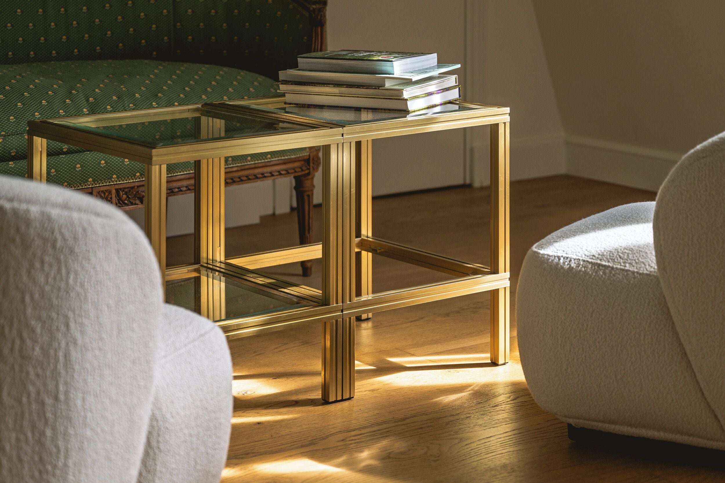 Une pièce comprenant une table d’appoint avec un plateau en verre, un canapé à motifs verts et un fauteuil blanc.