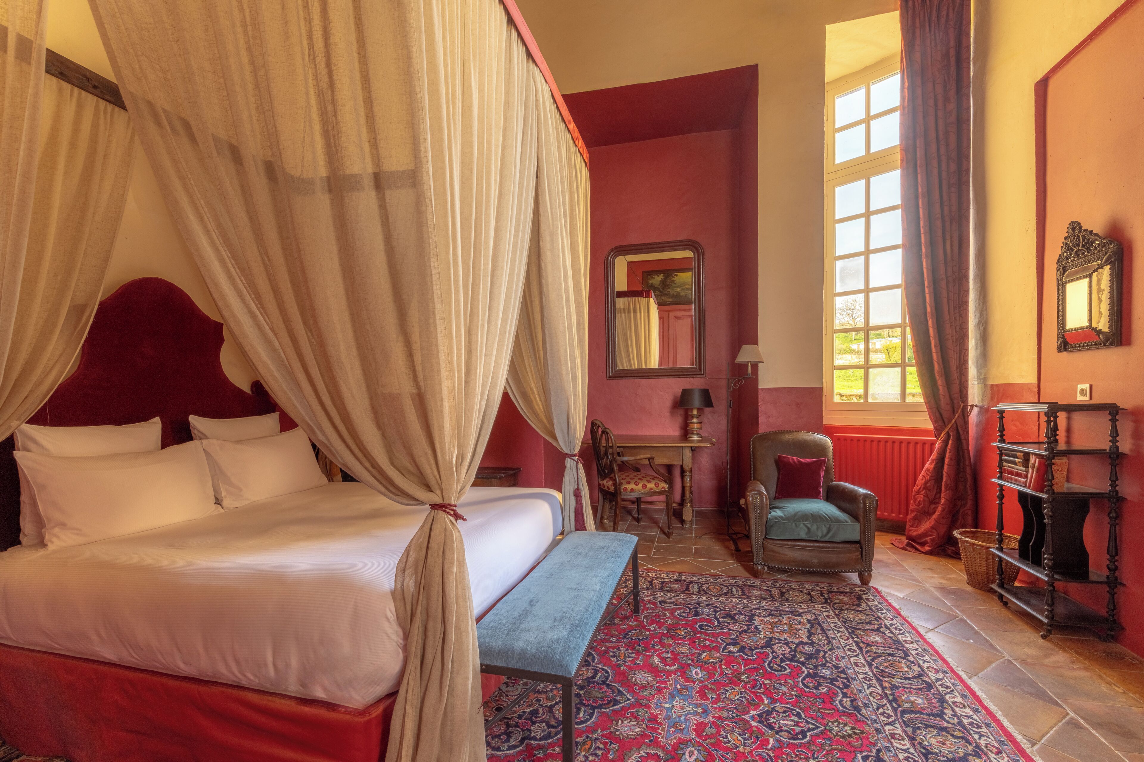 Una stanza con un letto a baldacchino, una poltrona, un tavolo e una libreria.
