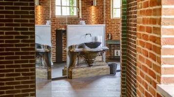 A bathroom with a brick wall, a large mirror, a sink with a bowl, and a wooden vanity.