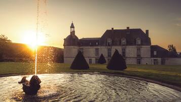 A large building with a fountain in the foreground and a sunset in the background.
