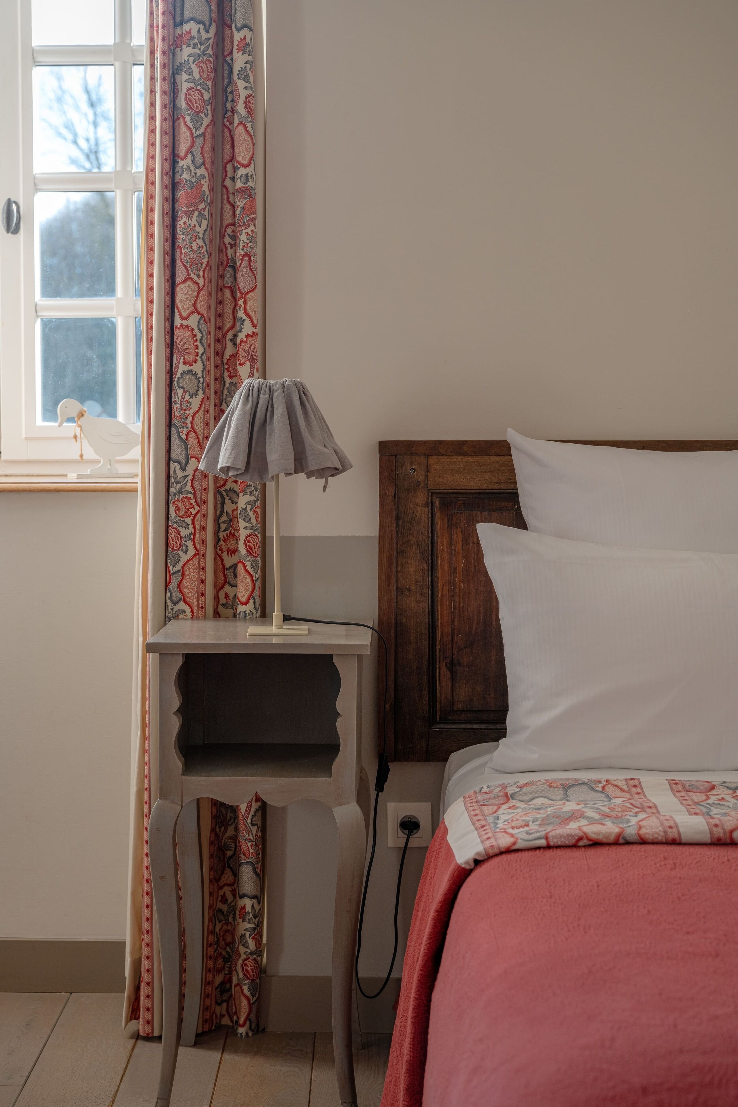 Une chambre à coucher avec une tête de lit en bois, une table de chevet avec une lampe, une couvre-lit à motifs et une fenêtre avec des rideaux.