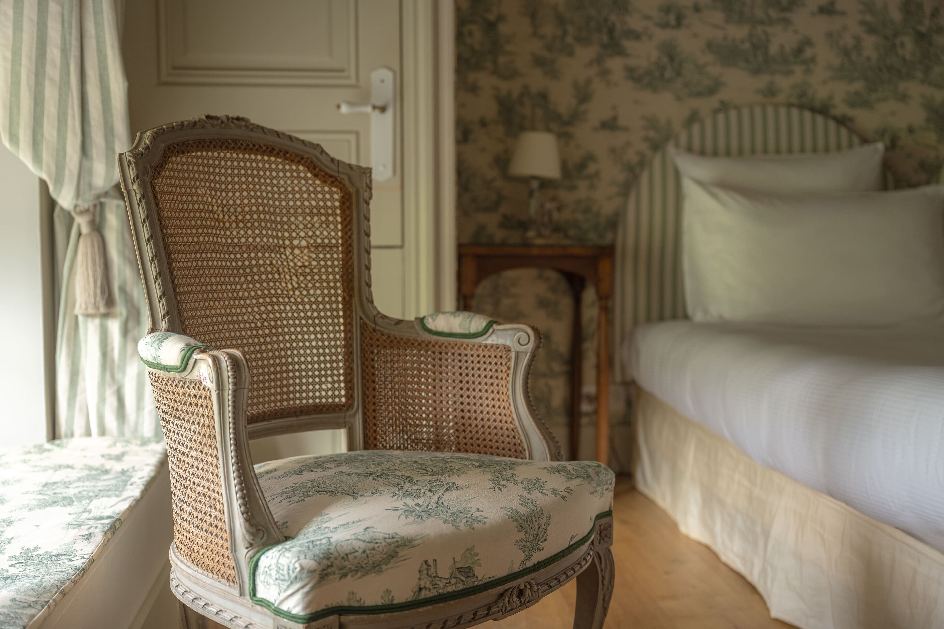 Une pièce comprenant un lit, une chaise à motifs floraux et une porte.