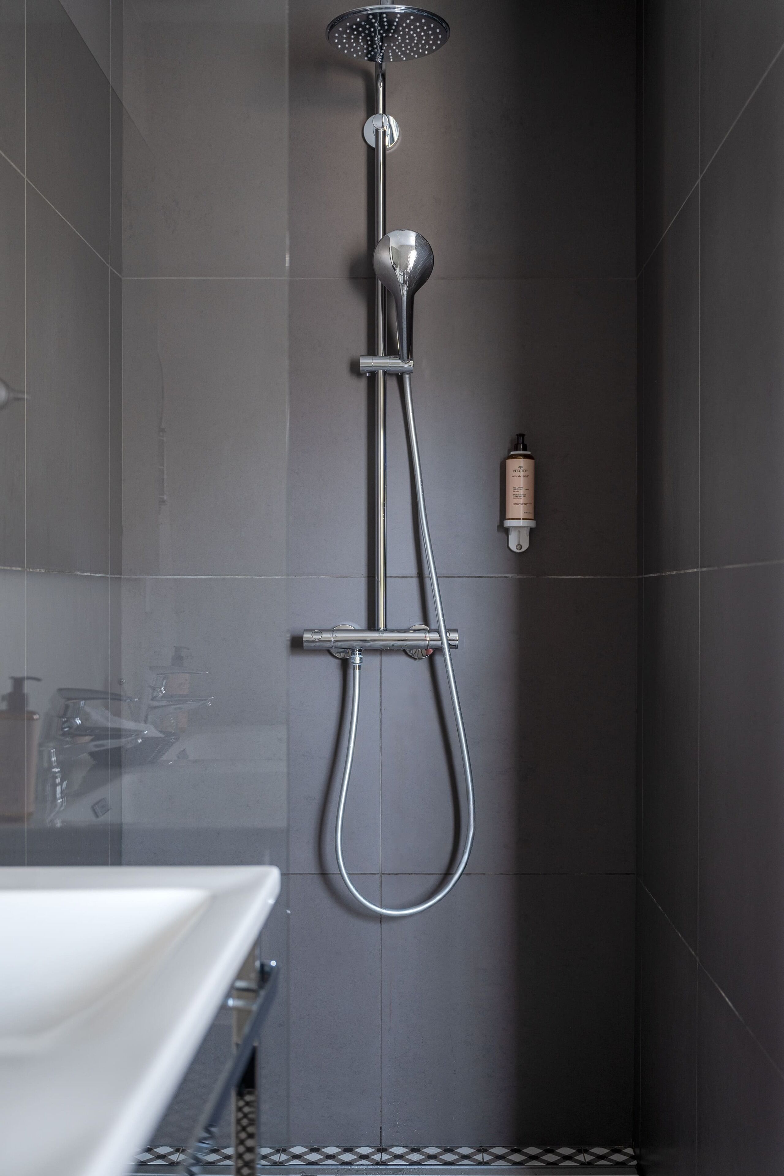 A modern bathroom with a shower, a sink, and a bottle of shampoo on the wall.