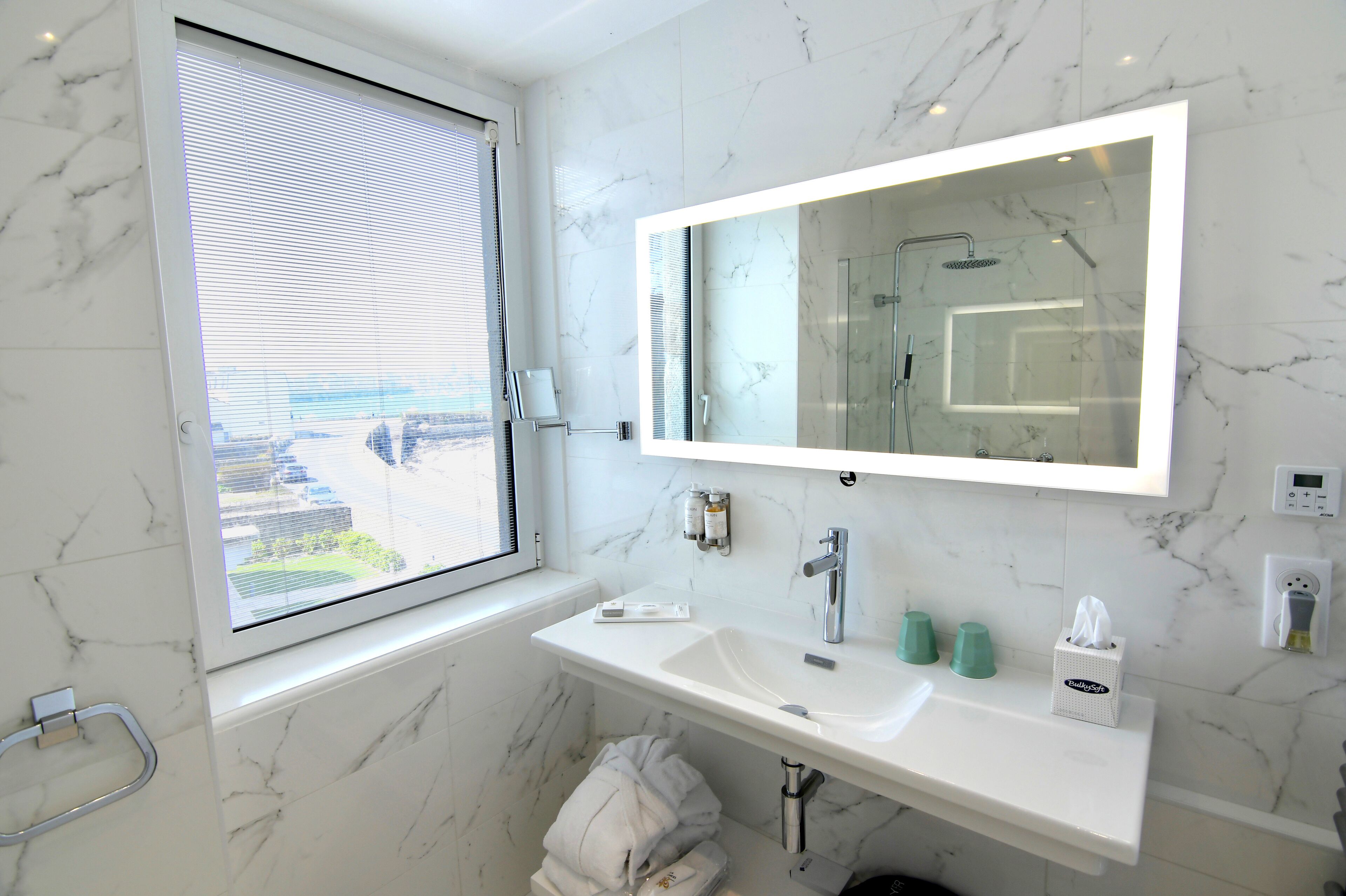 Un baño moderno con un espejo grande, un lavamanos y una ventana con persianas.