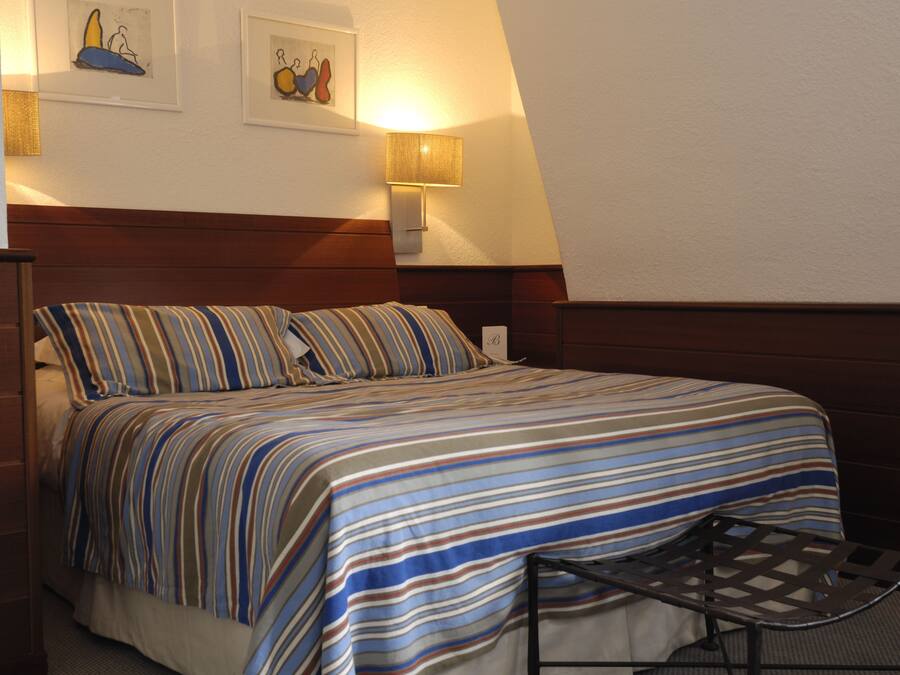 A neatly made bed with striped bedding, a bedside lamp, and two framed artworks on the wall.