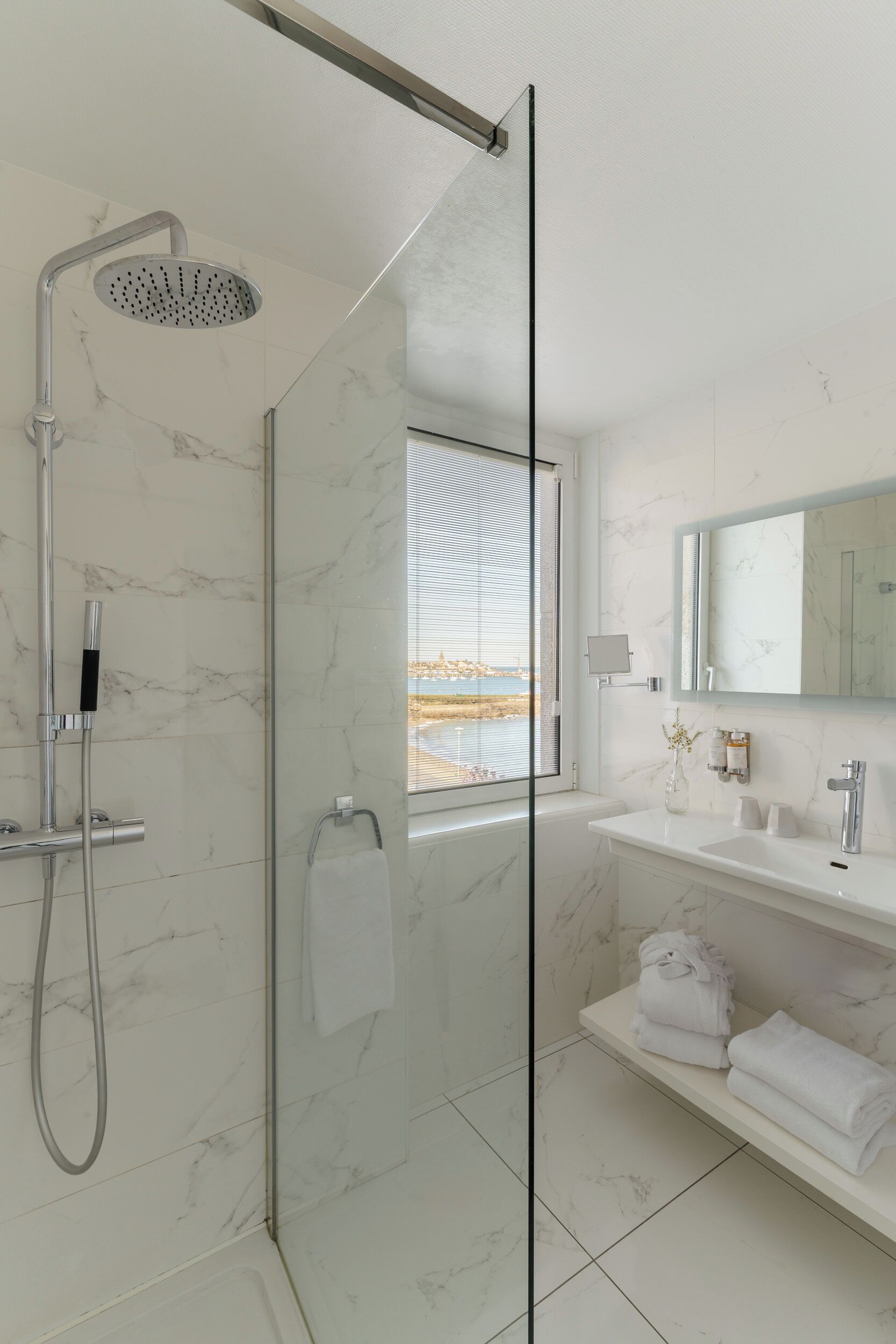 A modern bathroom with a glass shower enclosure, a white marble vanity, and a large mirror.