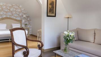 Une chambre à coucher avec un lit, une chaise en bois, un canapé, une table basse avec un livre, un vase de fleurs et un tableau encadré au mur.