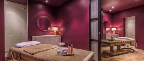 A spa room with a massage table, a vanity with a mirror, and a shower area.
