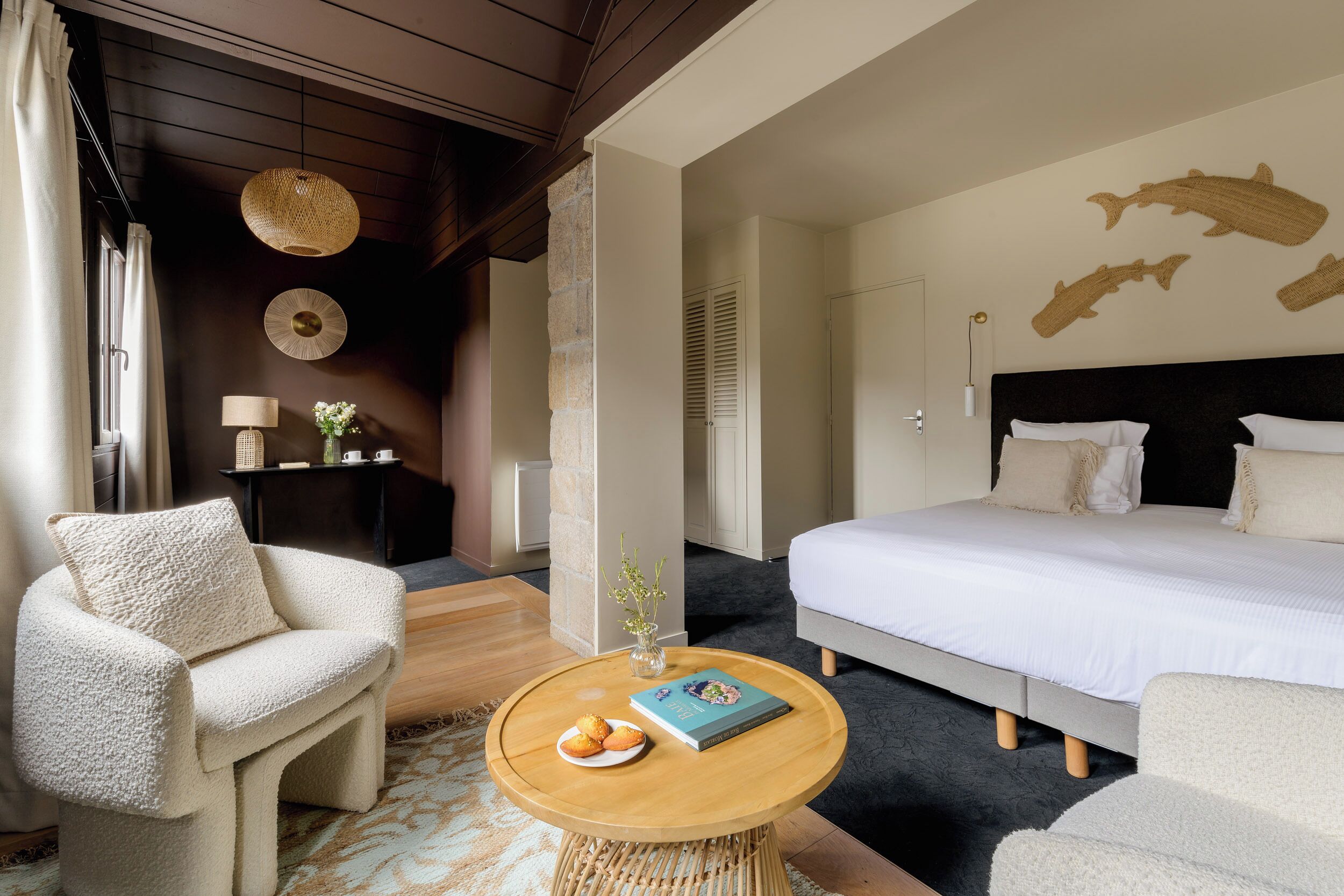 A bedroom with a bed, a round wooden table with a book and a plate of cookies, a chair, and a wall with shark artwork.