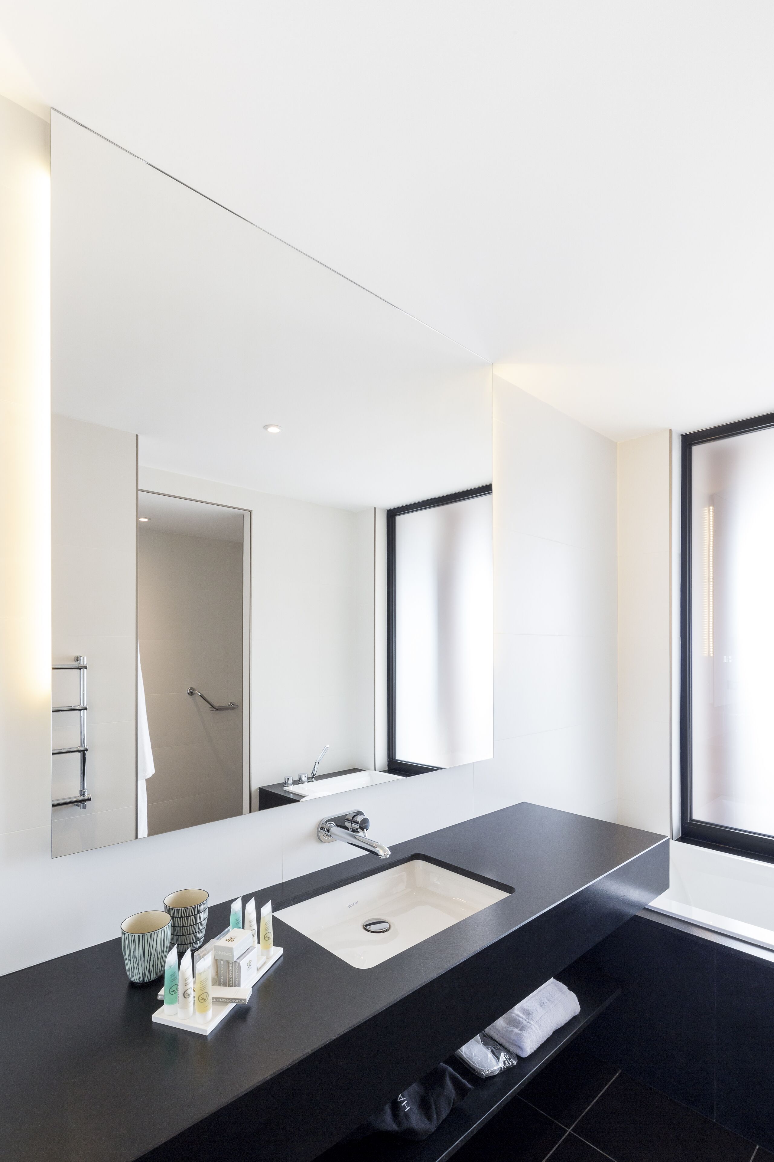 Une salle de bain moderne avec un grand miroir, un plan de toilette noir, un lavabo et une fenêtre.