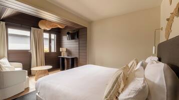 Un dormitorio con una cama grande, una mesita redonda pequeña, una silla y una ventana con cortinas.