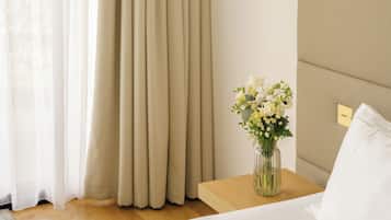 A bedroom with a bed, a nightstand, a vase with flowers, a lamp, and curtains.