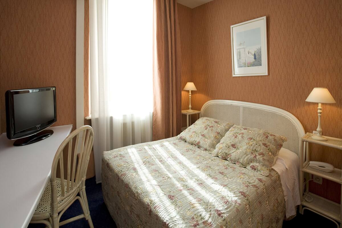 A hotel room with a bed, a desk, a chair, a television, and two bedside lamps.