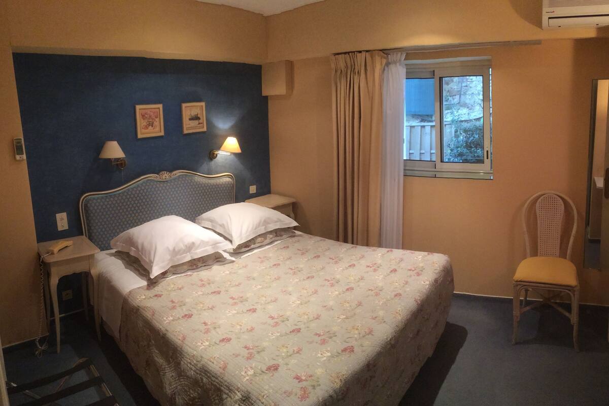 A hotel room with a bed, a nightstand, a chair, a window, and a door.