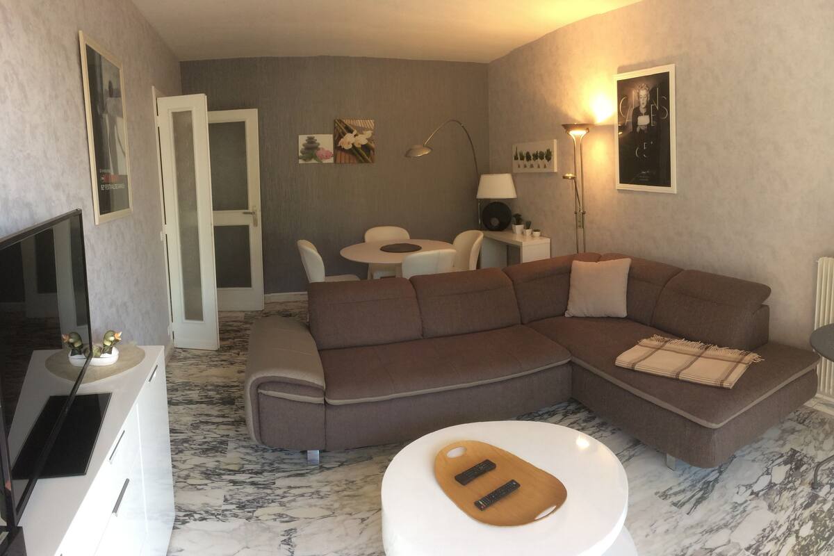 A modern living room with a sectional sofa, a small round table, a TV, and a lamp.