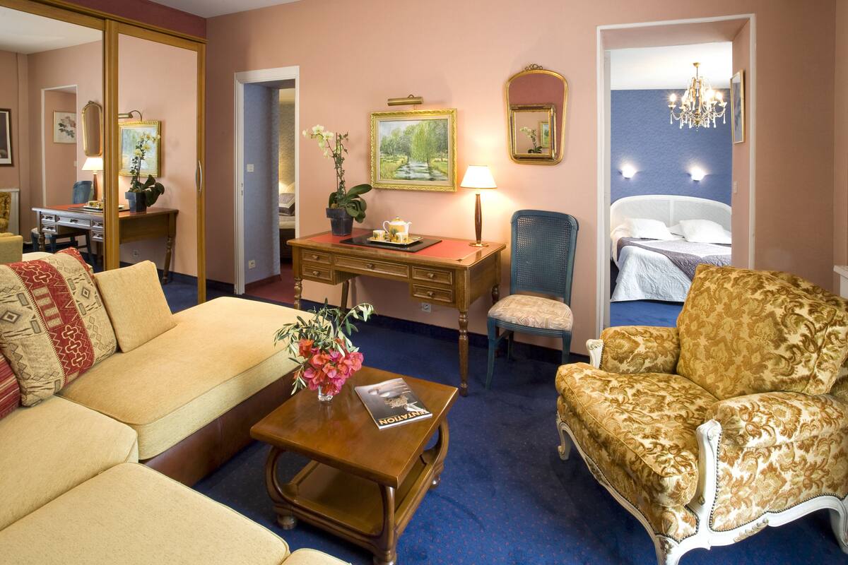 A hotel room with a sofa, armchair, desk, and a bed.