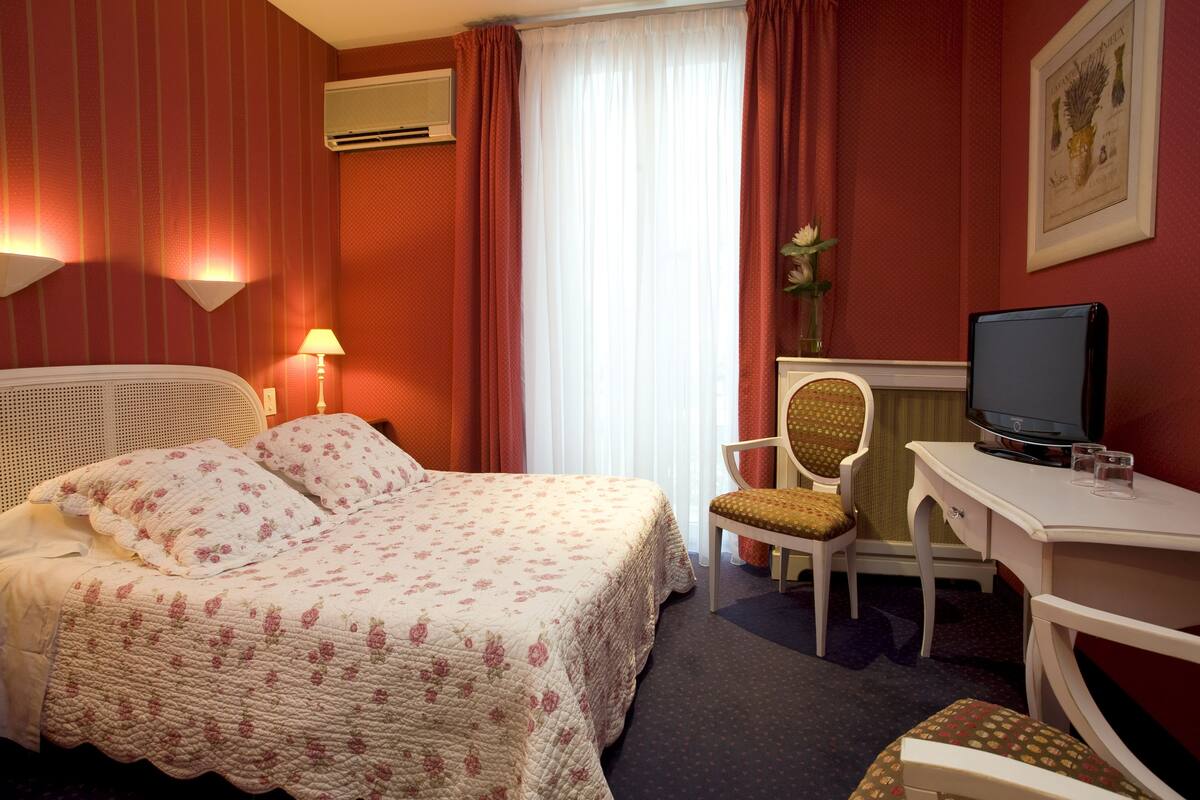 A hotel room with a bed, a desk with a television, a chair, and a lamp.