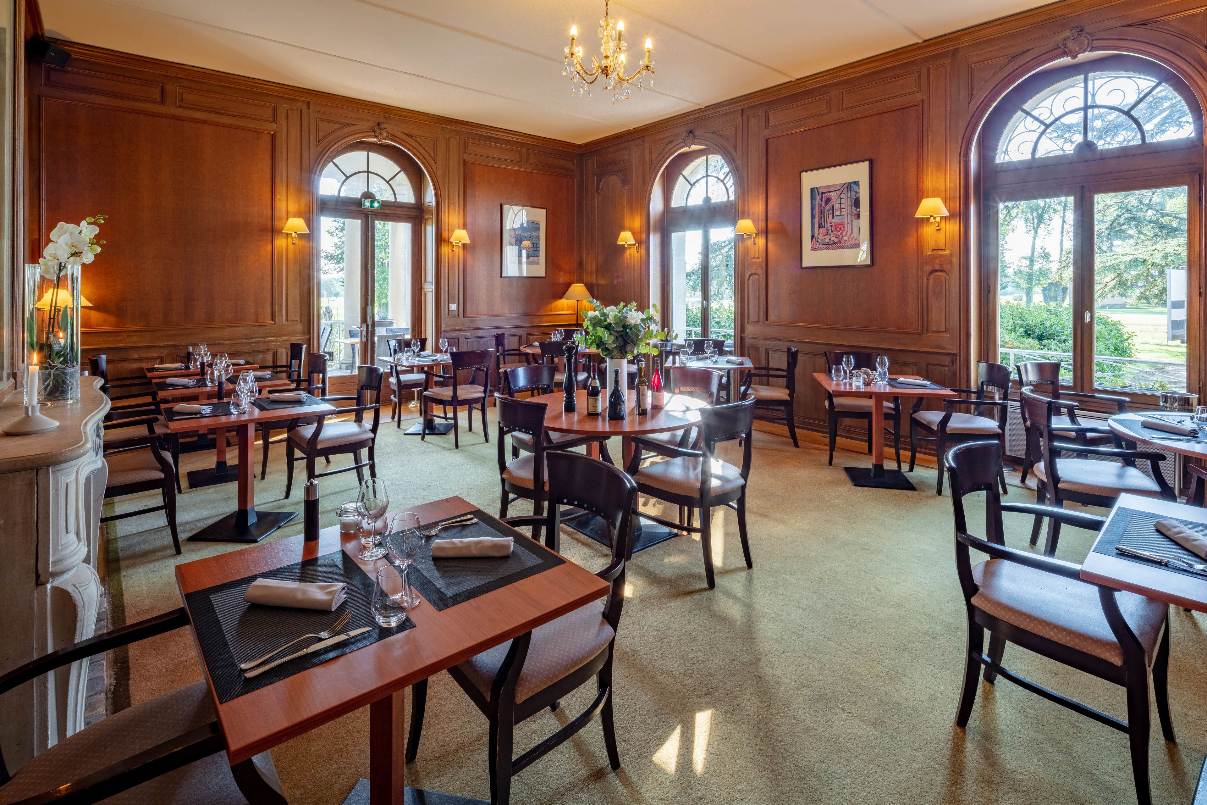A spacious dining area with wooden paneling, multiple tables and chairs, and large windows allowing natural light.
