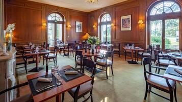 A spacious dining area with wooden paneling, multiple tables and chairs, and large windows allowing natural light.