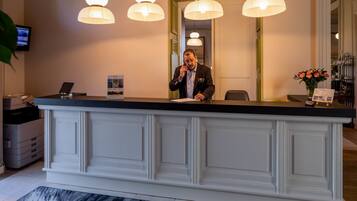 Een receptiebalie met een wit paneelontwerp, een digitaal scherm en een bloemetjesvaas.