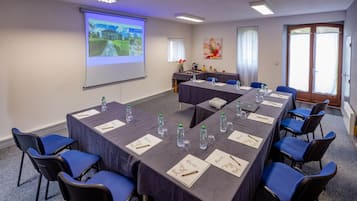 A conference room with long tables, blue chairs, and a projector screen displaying a landscape image.