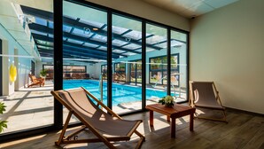 A room with large windows overlooking a swimming pool, wooden flooring, and two lounge chairs. - Garrigae Manoir de Beauvoir (Mignaloux-Beauvoir)