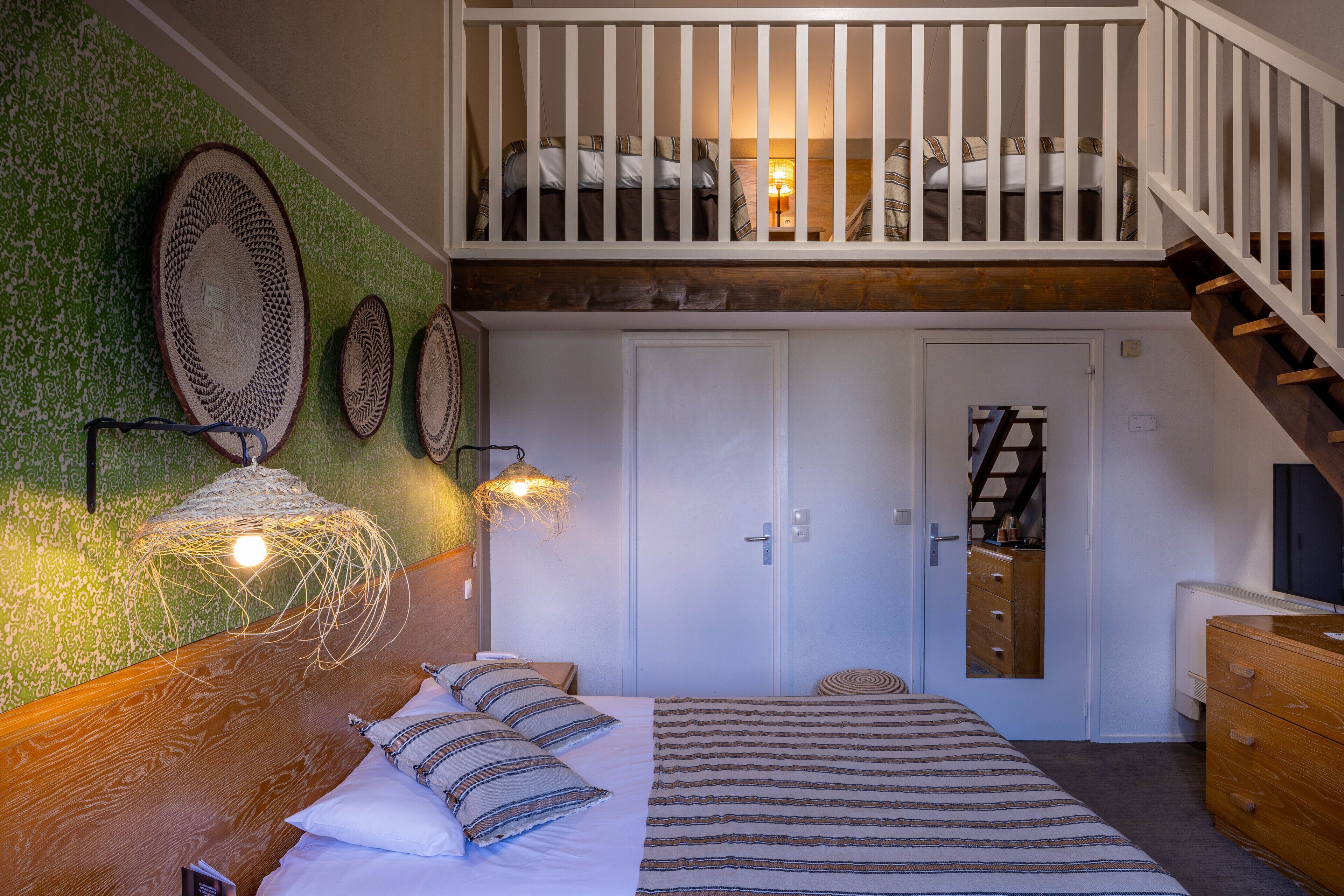 A bedroom with a bed, a wooden headboard, a green wall with woven decor, a white door, and a staircase.