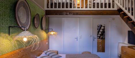 A bedroom with a bed, a wooden headboard, a green wall with woven decor, a white door, and a staircase.