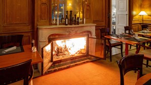 A warmly lit room with a fireplace, wooden furniture, and a table set for dining. - Garrigae Manoir de Beauvoir (Mignaloux-Beauvoir)