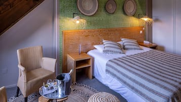 Un dormitorio con cabecera de madera, cama con ropa de cama a rayas, dos mesitas de noche, una silla de mimbre, una mesita redonda con una bandeja de vasos y una botella, y lámparas fijadas a la pared.