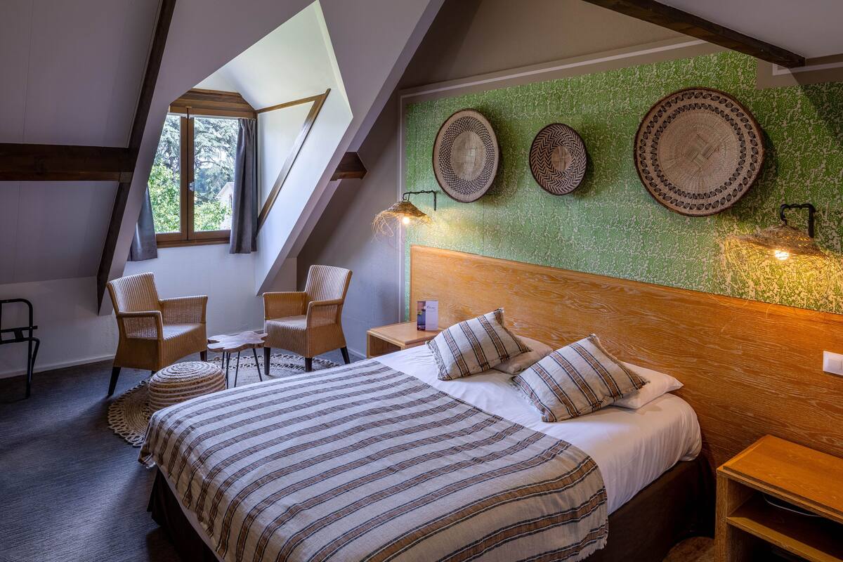 Une chambre avec un plafond en pente, un lit avec une literie à rayures, deux chaises, une petite table et trois assiettes décoratives accrochées au mur.