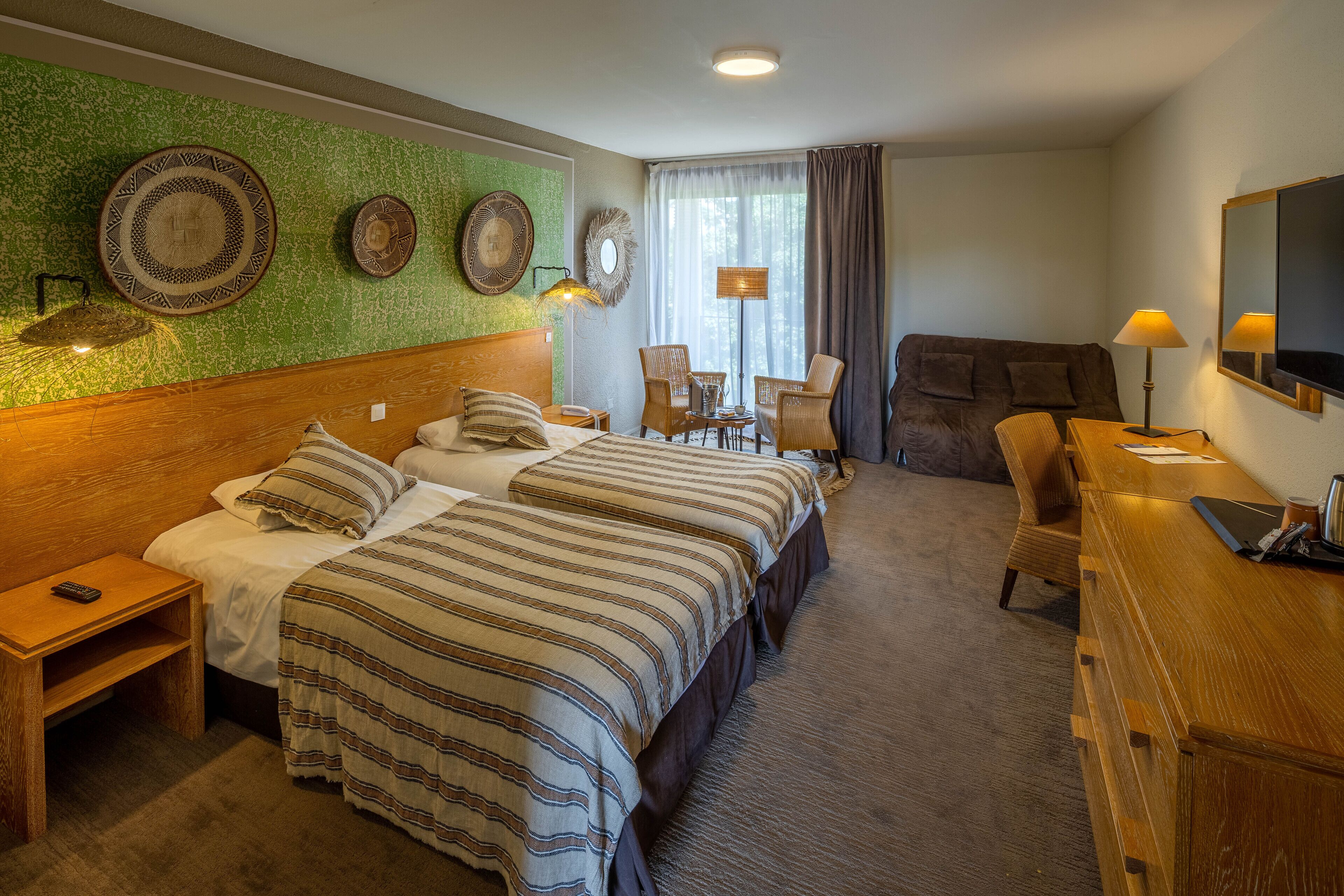 A hotel room with two beds, a desk, a chair, a TV, and a window with curtains.