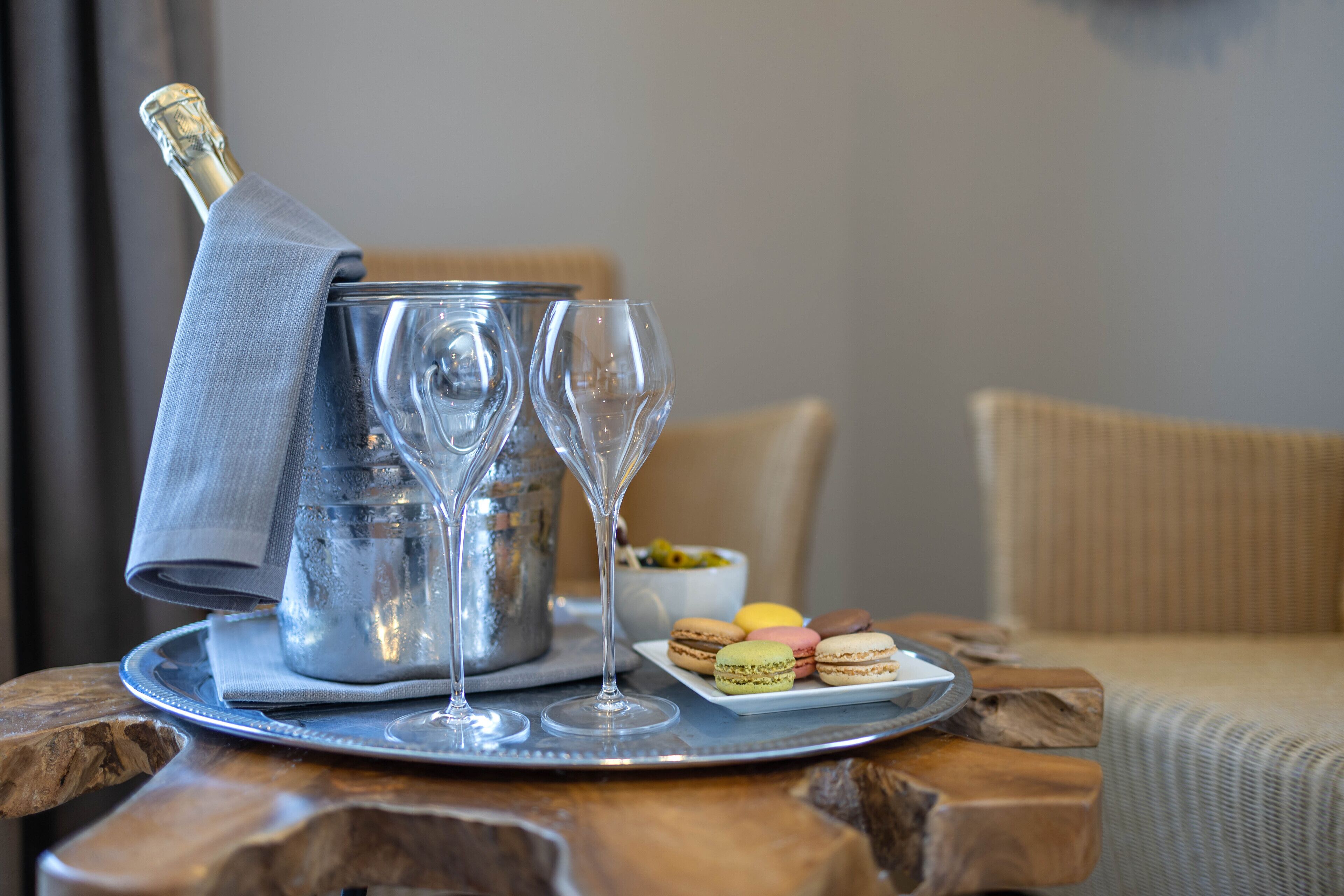 A tray with a champagne bottle, two glasses, and macarons on a wooden table.