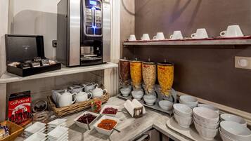 A hotel breakfast area with a coffee machine, tea station, and various breakfast items.