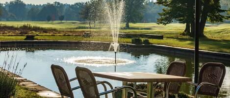 A patio with a table and chairs overlooking a pond with a fountain.