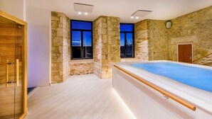 Un spa moderno con un amplio jacuzzi, paredes de piedra y ventanas grandes.