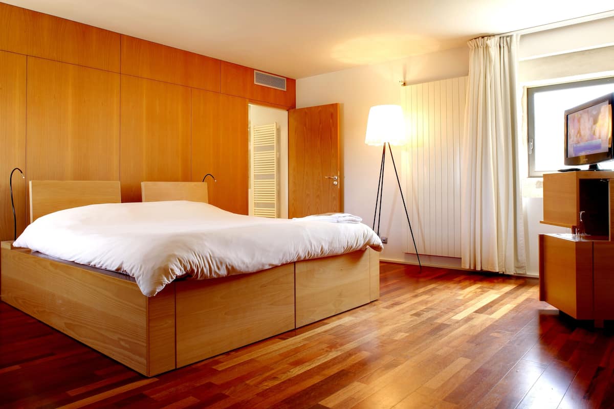 A modern hotel room with a wooden bed, a TV, and a desk.