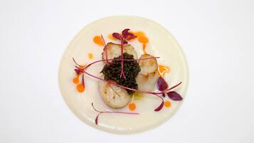 Une assiette de mets comprenant des Saint-Jacques poêlées, du caviar et diverses garnitures.