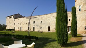 Un edificio de piedra con un patio, mesas al aire libre y altos cipreses.