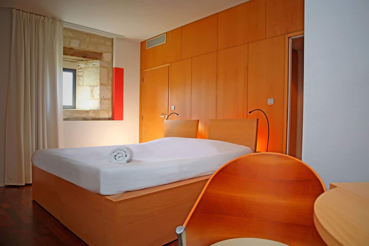 A hotel room with a wooden bed, a wooden chair, and a window with a view of the outside.