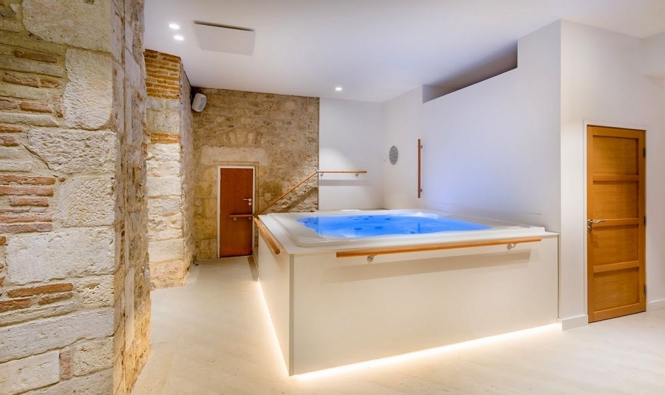 A modern bathroom with a stone wall, a wooden door, and a white bathtub.