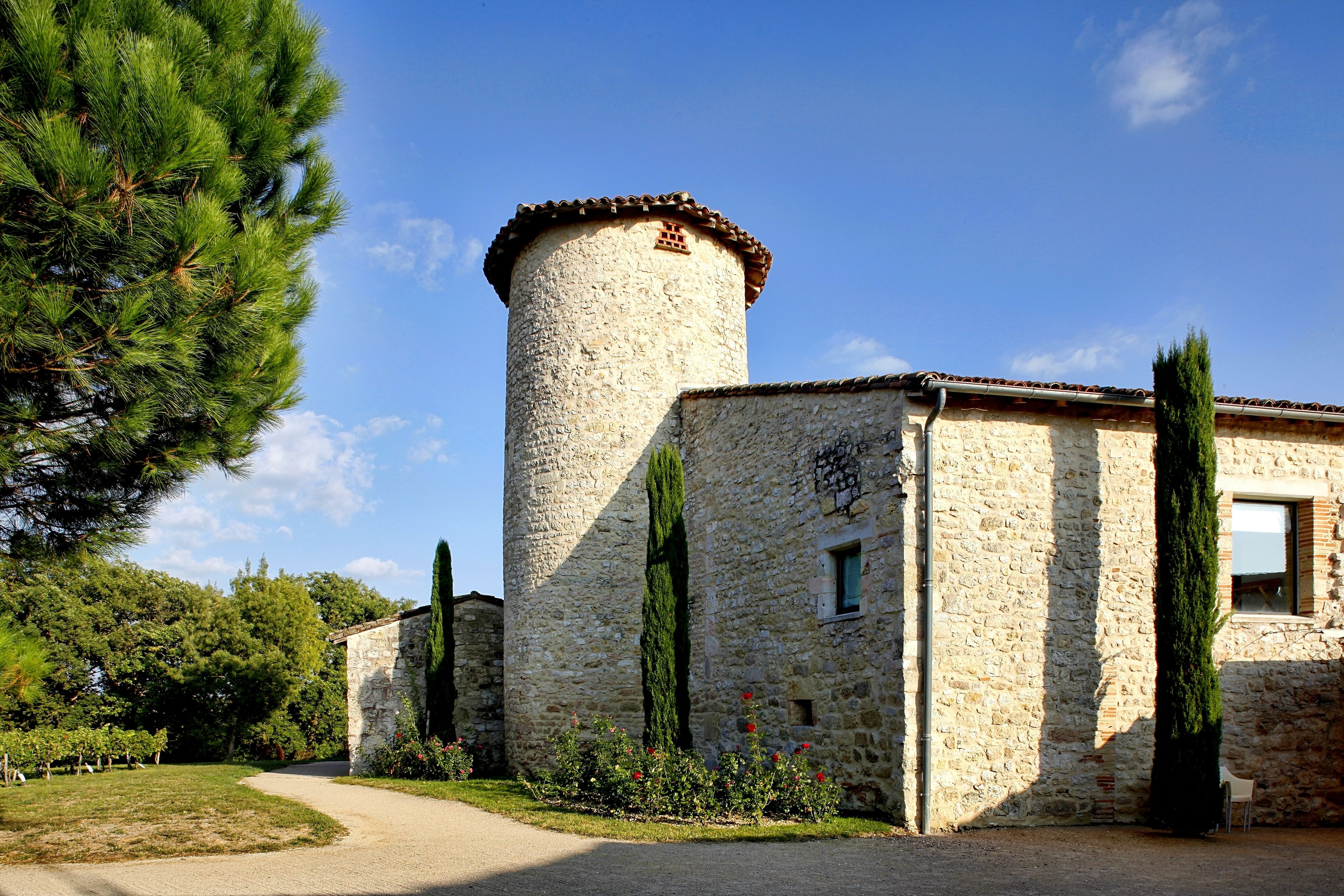 A stone building with a tower, surrounded by greenery and a gravel path.